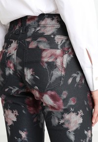 Jeans en denim à imprimé floral gris foncé avec des accents roses, dotés de poches arrière et d'un design standard à cinq poches. Texture de denim lisse.