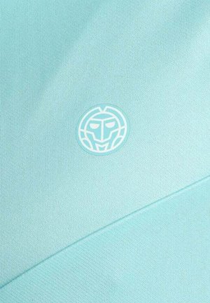 Hellblauer Stoff mit einem kleinen, runden, stilisierten Maskenlogo in Weiß und Türkis, das mittig auf der Oberfläche platziert ist.