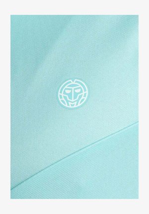 Hellblauer Stoff mit einem kleinen, runden, stilisierten Maskenlogo in Weiß und Türkis, das mittig auf der Oberfläche platziert ist.