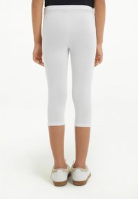 Leggings blancs en coton avec une coupe ajustée, longueur cropped et une taille douce. Portés avec des baskets blanches à semelle en gomme.