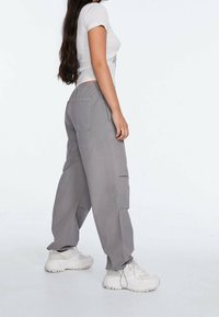 Baggy grijze cargo-broeken met zijzakken, gemaakt van lichtgewicht stof; gedragen met een aansluitend wit topje en chunky witte sneakers.