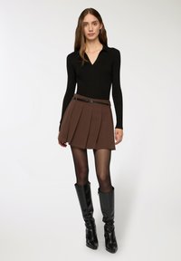 Top aderente nero a maniche lunghe, gonna mini plissettata marrone con cintura nera, stivali alti fino al ginocchio neri con tacco, texture lisce, design minimalista.