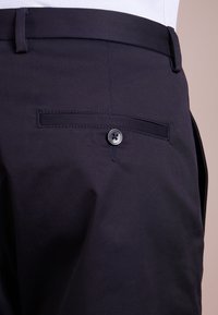 Marineblauwe broek met een gladde textuur, voorzien van een enkele achterzak met knoopsluiting en een nette, op maat gemaakte uitstraling.