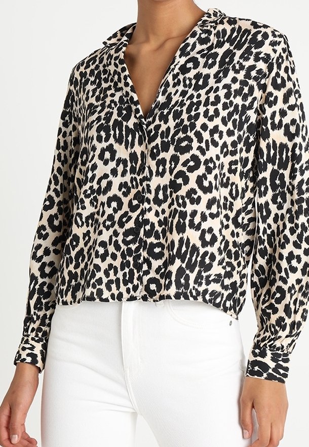 Camicia a bottoni con stampa leopardata in tessuto leggero, dotata di colletto, maniche lunghe e orlo corto. Indossata con jeans bianchi.