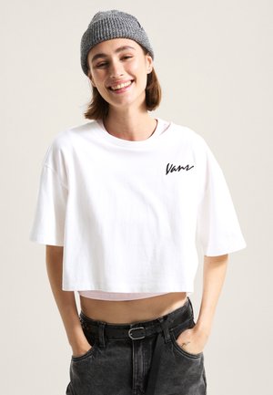 White cropped t-shirt with short sleeves and "Vans" logo in black. Paired with high-waisted dark jeans and a gray knit beanie.