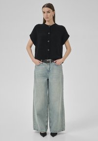 Black, boxy knit top with short sleeves and five buttons paired with light-wash, wide-leg jeans and black pointed-toe shoes.