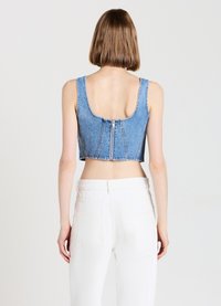 Cropped top in denim blu con schiena bassa e chiusura con zip, caratterizzato da spalline larghe e un design aderente, abbinato a pantaloni bianchi a vita alta.