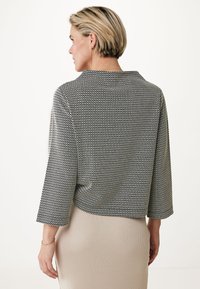 Černobílá vzorovaná bunda s cropped střihem, širokými rukávy a klasickým límcem, spárovaná s žebrovanou béžovou sukní.