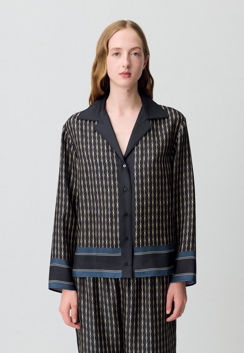 Camicia da pigiama nera in satin con motivo a catena, chiusura a bottoni, e strisce blu in contrasto all'orlo e ai polsini, con colletto classico.