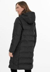 Sort oppustelig jakke med hætte, der har et quiltet design og en mellem-lang længde. Glat, vandafvisende materiale med en glat overflade.