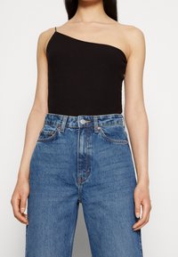 Haut noir côtelé à une épaule associé à un jean en denim bleu clair taille haute, coupe droite classique avec des surpiqûres contrastantes.