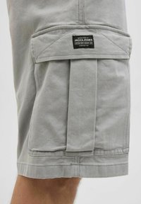 Grau Baumwollshorts mit einer vorderen Falte, einer aufgesetzten Tasche mit Klappe und einem schwarzen Etikett. Der Saum ist ordentlich genäht für Langlebigkeit.