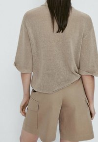 Knit beige sweater with short sleeves and a loose fit, paired with tan shorts featuring side pockets and a textured fabric.