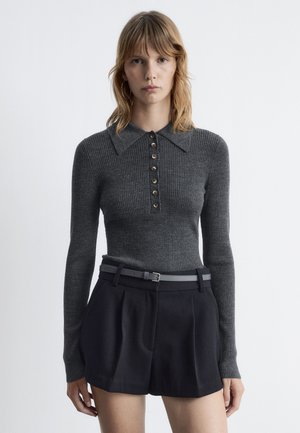 Gray ribbed long-sleeve top with a pointed collar and button placket, paired with high-waisted black shorts and a gray belt.