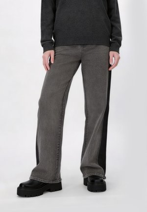 Persona che indossa jeans larghi neri sbiaditi con pannelli laterali neri, stivali neri con suola platform spessa e un maglione grigio scuro.