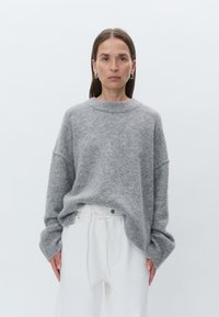 Suéter cinza de tamanho oversized em material suave, com decote redondo e punhos canelados, combinado com calças brancas de cintura alta.