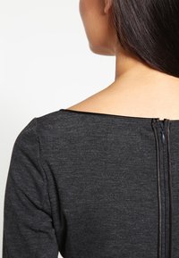 Tmavě šedý přiléhavý top s širokým výstřihem, texturovanou látkou a diskrétním zipem vzadu. Hladký, minimalistický design.