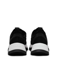 Paire de baskets athlétiques noires et blanches vues de dos, avec une tige noire et une semelle intermédiaire blanche épaisse avec le nom de la marque en relief.