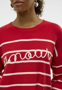 Pull rouge avec des rayures horizontales blanches, comportant un motif de texte en relief "amour". Col côtelé, texture douce, détails de couture visibles.