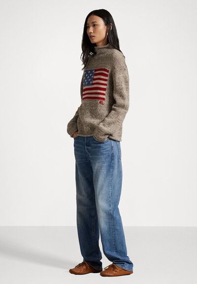 Hnedý pletený sveter s veľkým dizajnom americkej vlajky v červenej a modrej farbe. Skombinovaný s svetlomodrými džínsami a hnedými topánkami.