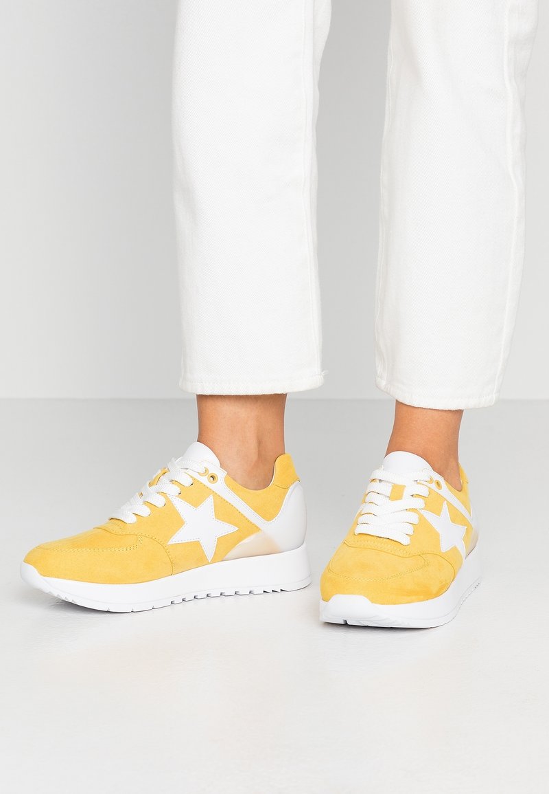 Baskets en daim jaune avec des accents blancs, arborant un motif étoile, des lacets blancs et une semelle en caoutchouc texturée.