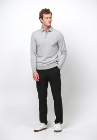 Ljusgrå långärmad polo med en tre-knapplång placket, kombinerad med svarta byxor och vita sneakers. Enkel, avslappnad design.