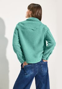 Pull en polaire turquoise au toucher doux, coupe oversize et col rabattu. Associé à un jean en denim foncé taille haute.