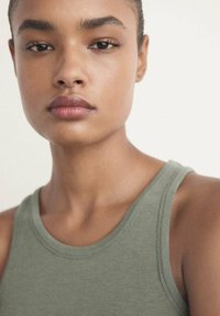 Lys grøn tanktop med rund hals, udført i glat stof og en tætsiddende design, båret af en model med kort hår.