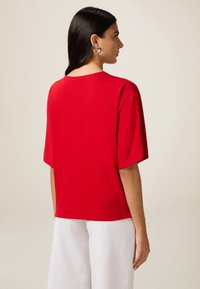 T-shirt en coton rouge avec une coupe décontractée et des manches courtes, mettant en avant un col rond et une texture lisse. La vue de dos montre une longueur jusqu'aux épaules.