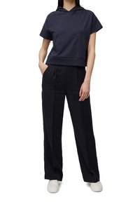 Sudadera cropped en azul marino con un bolsillo frontal y mangas cortas, combinada con pantalones sueltos en azul marino. Zapatillas blancas completan el atuendo.
