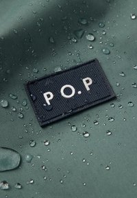 Groene waterdichte stof met druppels; beschikt over een textuurgepatchte marineblauwe rechthoekige patch met "P.O.P" in witte letters.