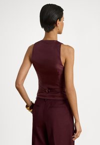 Μπορντό αμάνικη μπλούζα με ομαλή υφή, εφαρμοστή σχεδίαση και πλαϊνή λεπτομέρεια με πόρπη, σε συνδυασμό με ταιριαστό παντελόνι.