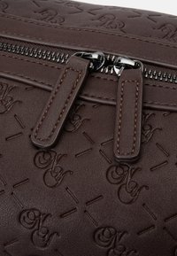 Brown leather bag featuring an embossed pattern, dual zippers with chrome accents, and tan stitching detail on the zipper pulls.