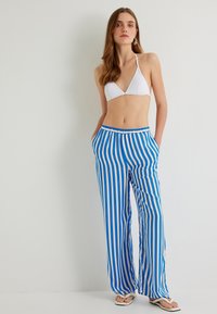 Witte driehoek bikini-top gecombineerd met blauw-witte gestreepte wijde broek. De broek heeft een tailleband met koord en zijkanten met zakken.