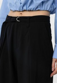 Black high-waisted trousers with a fabric texture, featuring a silver D-ring belt and side pockets, paired with a light blue blouse.