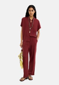 Bordowa koszula z krótkim rękawem i dopasowane luźne spodnie, połączone z paskowaną żółtą torbą i prostymi klapkami, tworzą swobodny wygląd.