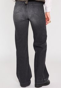 Jeans évasés noirs avec un délavage, présentant un design à cinq poches, des coutures contrastantes et une texture en denim lisse.