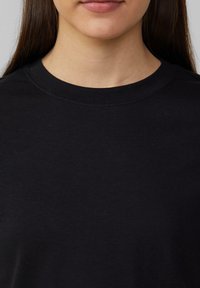 Černé bavlněné tričko s kulatým výstřihem. Látka působí měkce, s hladkou strukturou a minimálním prošitím okolo límce.