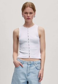 Weißes geripptes Tanktop mit Rundhalsausschnitt und Knopfdetaillierung an der Vorderseite. Kombiniert mit hellblauen high-waisted Jeans.