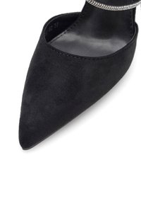 Fekete velúr hegyes orrú cipő sima felülettel és díszes kristály kiemeléssel a bokapánton. Lapos talp, minimális bordázattal.