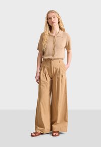Haut à manches courtes avec boutons en ribbed beige, associé à un pantalon large à taille haute beige et des sandales plates marron. Tissu doux et design structuré.