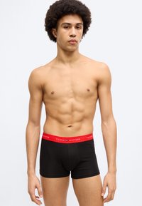 Μαύρα βαμβακερά μπόξερ με κόκκινη ζώνη μέσης που φέρει το λογότυπο "TOMMY HILFIGER". Ομαλή υφή, εφαρμοσ τή σχεδίαση και μέτριο ύψος μέσης.