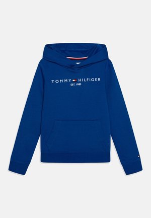 Sweat à capuche bleu Tommy Hilfiger avec poche avant, texte logo "TOMMY HILFIGER EST. 1985" et petit emblème de drapeau sur le poignet de la manche gauche.