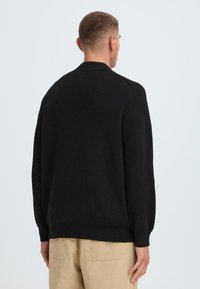 Schwarzer Strickpullover mit geripptem Kragen und Bündchen. Verfügt über eine lockere Passform und eine glatte Textur. Trägt man über hellen Hosen.