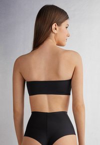 Sort bandeau crop top kombineret med højhalsede bund; glat tekstur, sømløst design, minimalistisk stil og ingen synlig hardware.