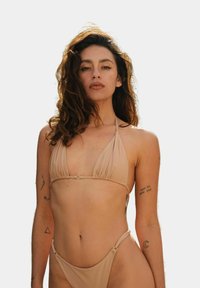 Beżowy bikini z halterem, wyposażone w trójkątne miseczki i minimalne zakrycie. Gładka tekstura z zapięciem z tyłu.