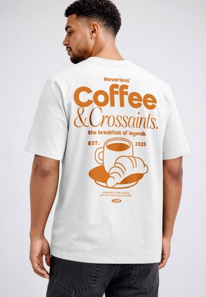 Mann trägt weißes T-Shirt mit orangem Text und Grafik einer Kaffeetasse und einem Croissant auf dem Rücken, bewirbt das Frühstück „Coffee & Croissants“.