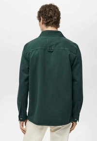 Chemise à manches longues vert foncé avec col, poignets à boutons et ourlet droit. Texture unie avec un détail d'empiècement au dos.