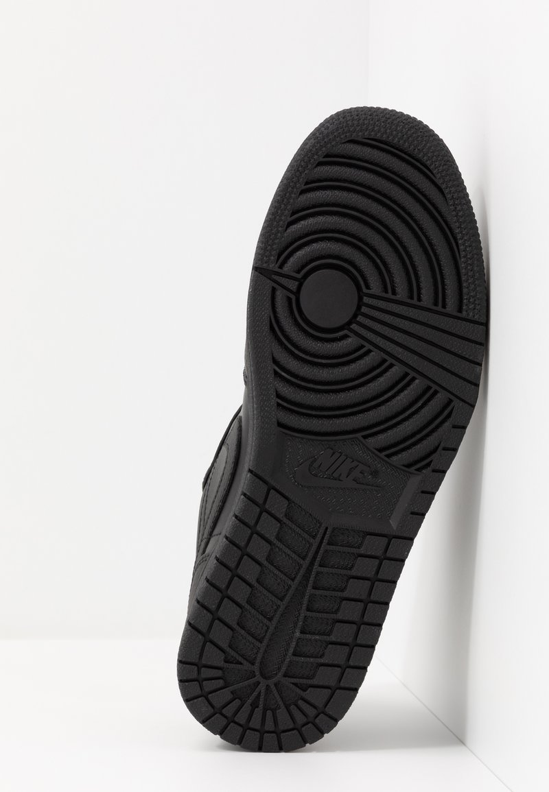 Schwarze Sneaker-Sohle mit tiefem Profilmuster, mit kreisförmigen Akzenten und eingeprägtem "Nike"-Logo. Glattes Gummimaterial, robuste Konstruktion.