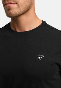 Black cotton t-shirt with crew neck, short sleeves, and white 'EST. 1983' logo. Smooth texture and fitted design, visible stitching on shoulders.